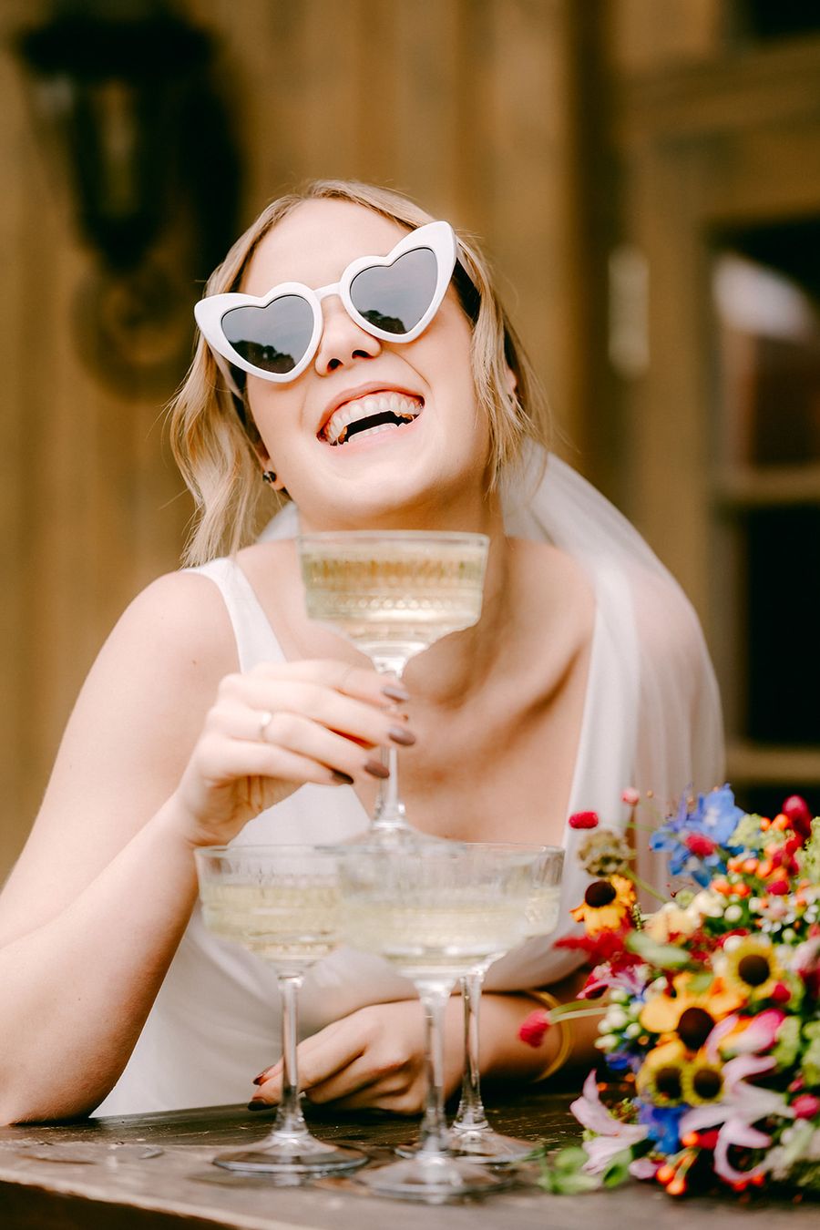 Cheers to the bride lachenden Braut mit Herz-Sonnenbrille und buntem Blumenstrauß