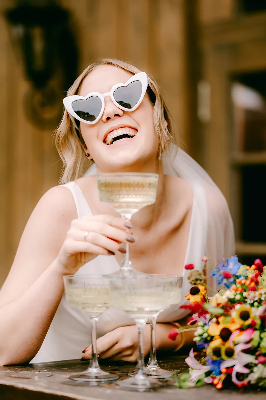 lachenden Braut mit Herz-Sonnenbrille und buntem Blumenstrauß